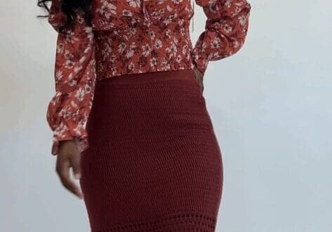 A woman stands against a plain background wearing a red floral long-sleeve top, a red crochet midi skirt, and heeled sandals.