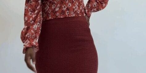A woman stands against a plain background wearing a red floral long-sleeve top, a red crochet midi skirt, and heeled sandals.