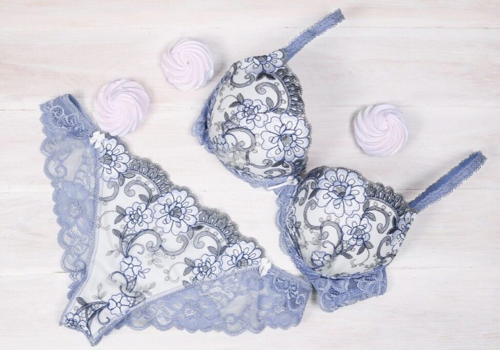 A matching lace bra and panties set in lavender and white is arranged on a white wooden surface with three pink meringue cookies.