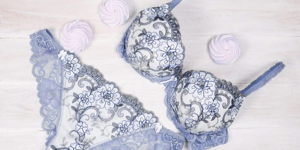 A matching lace bra and panties set in lavender and white is arranged on a white wooden surface with three pink meringue cookies.