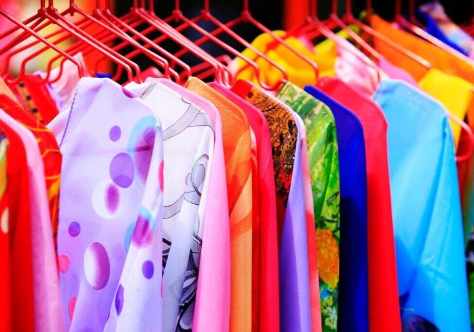 Colorful shirts and dresses on red hangers are displayed on a clothing rack, showcasing a variety of patterns and fabrics.