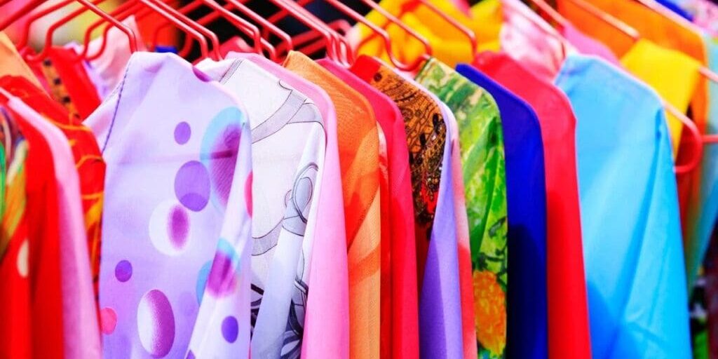 Colorful shirts and dresses on red hangers are displayed on a clothing rack, showcasing a variety of patterns and fabrics.