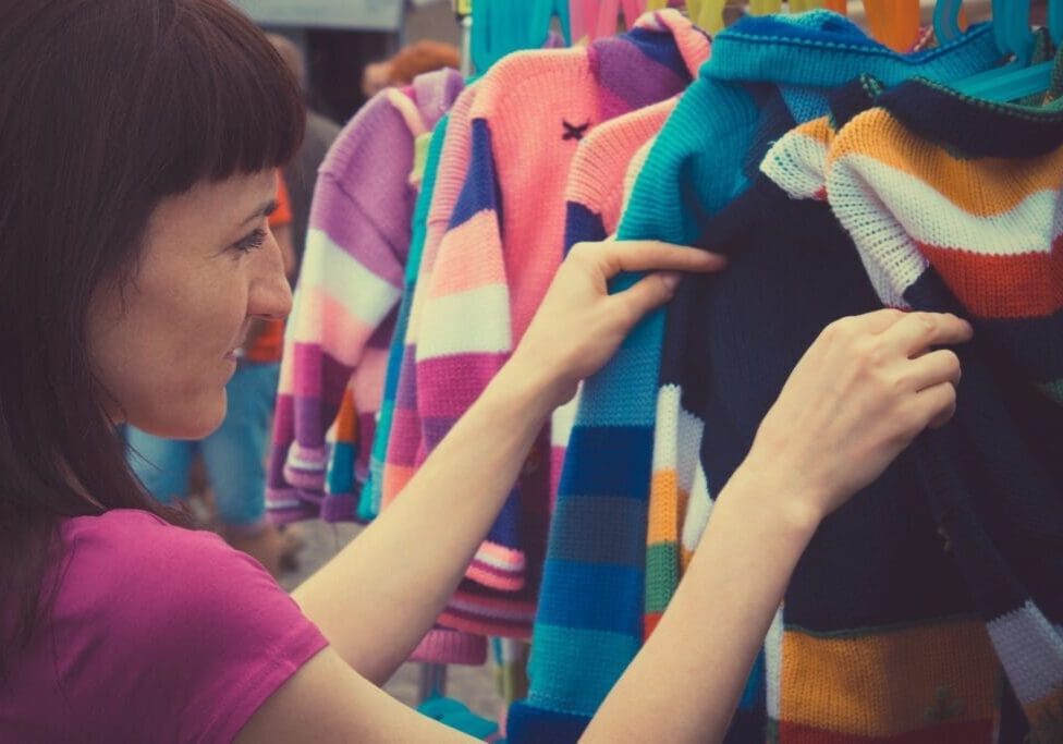 A woman examines colorful striped sweaters on a clothing rack.