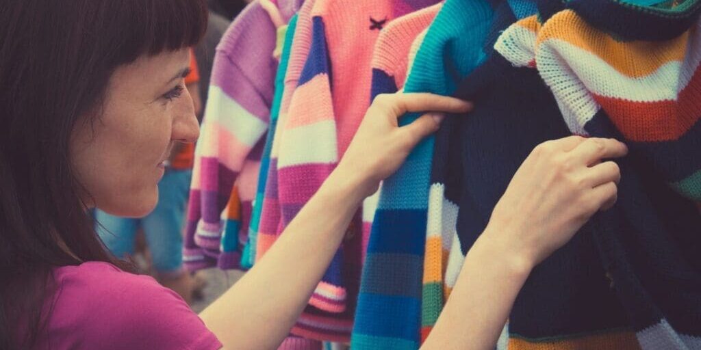 A woman examines colorful striped sweaters on a clothing rack.